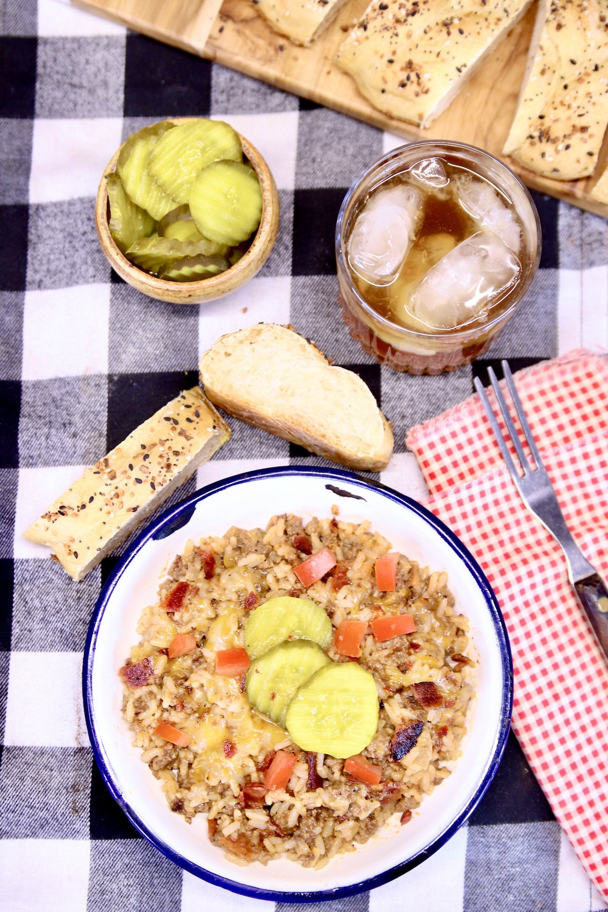 bacon cheeseburger rice in a bowl with pickles. Glass of tea, 2 slices of bread, pickles in a bowl.