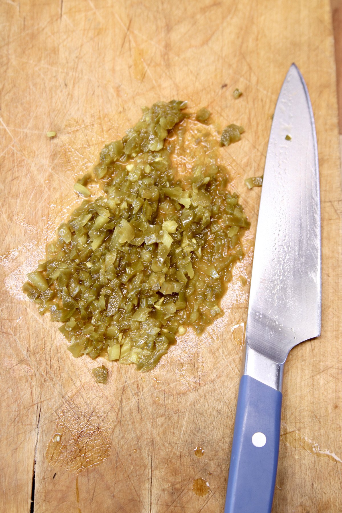 diced pickled jalapenos on a cutting board with knife
