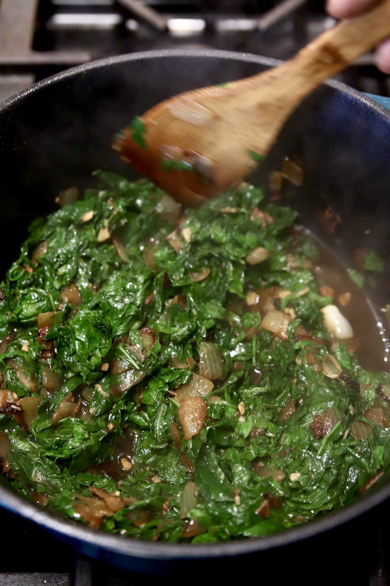 wilted turnip greens in a pan with wood spoon