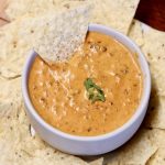 Chili Cheese Dip in a bowl with a tortilla chip dipping