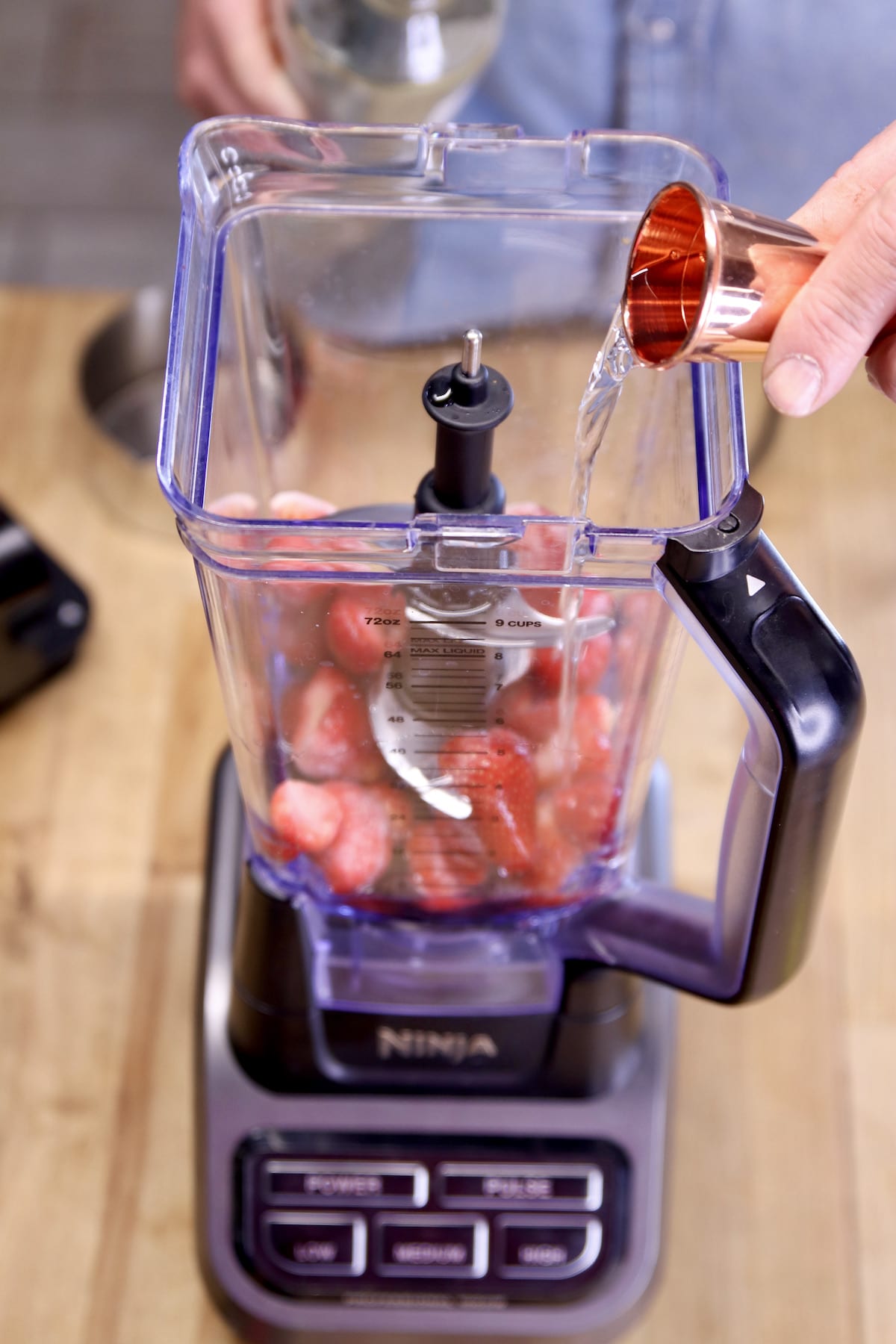 adding vodka to a blender with strawberries.