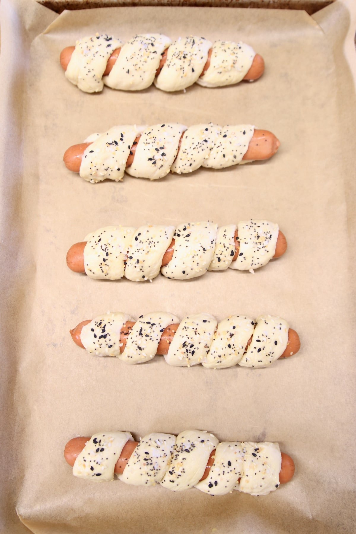 pretzel dogs on a parchment lined baking sheet - ready to bake.