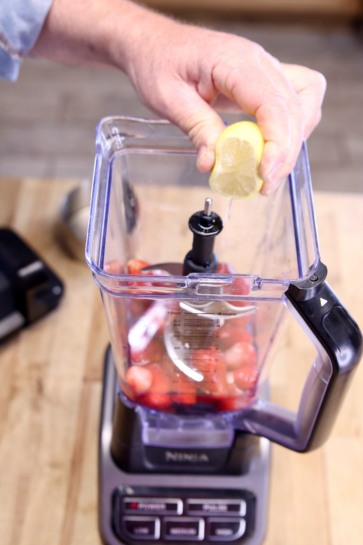 squeezing half a lemon into blender with strawberries.