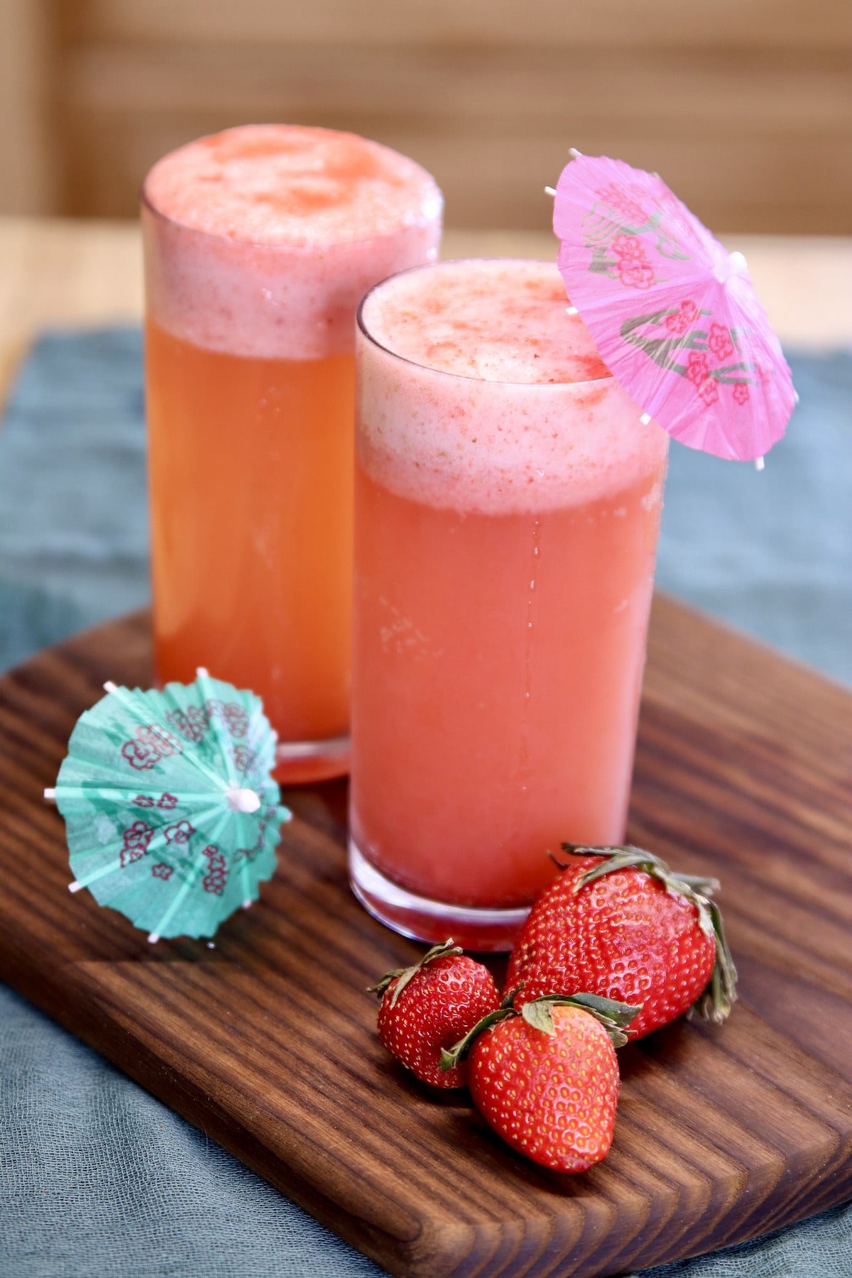2 glasses of strawberry shandy cocktails with fresh strawberries and drink umbrellas.