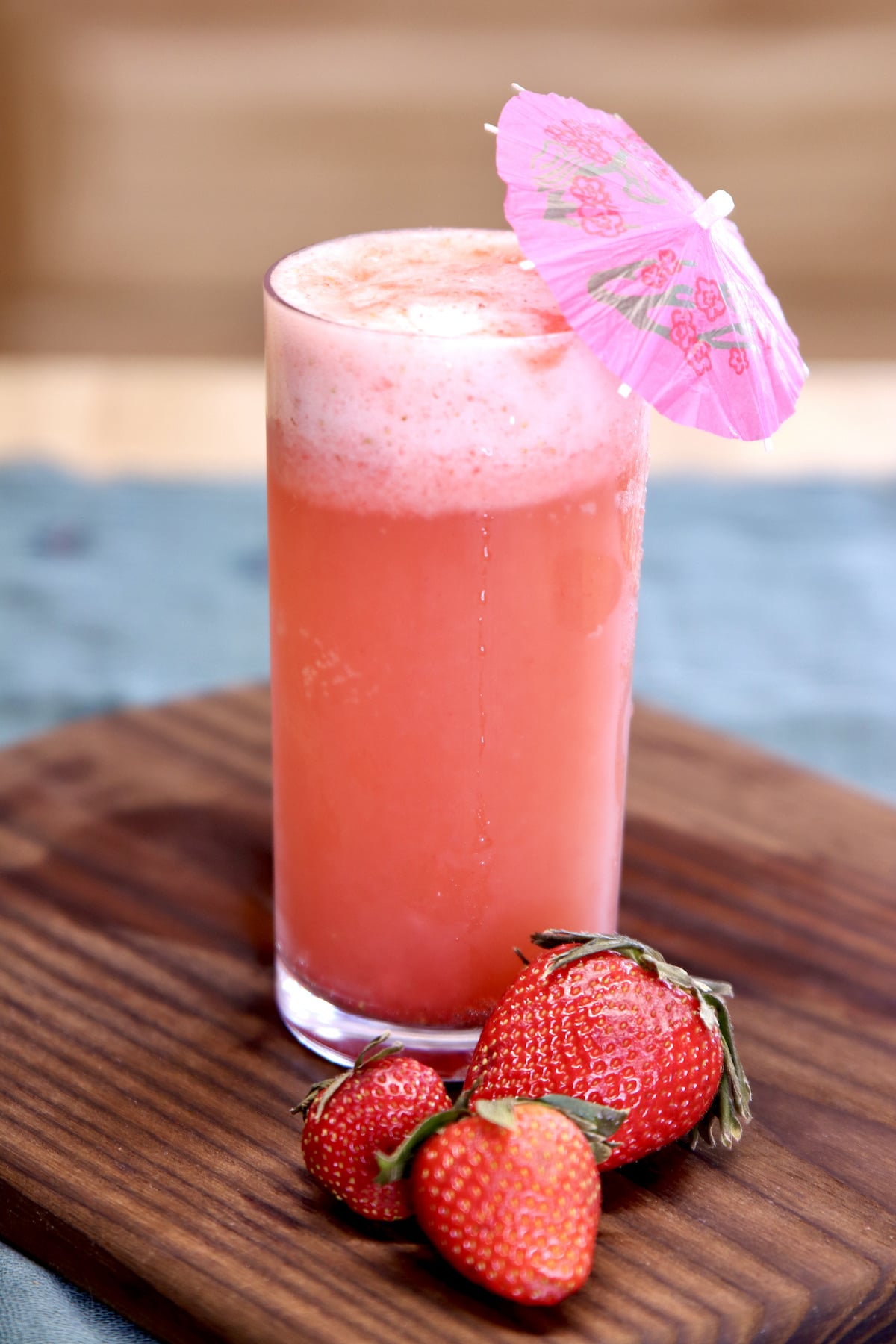Strawberry Shandy Cocktail with drink umbrella and 3 fresh strawberries in front of the glass.