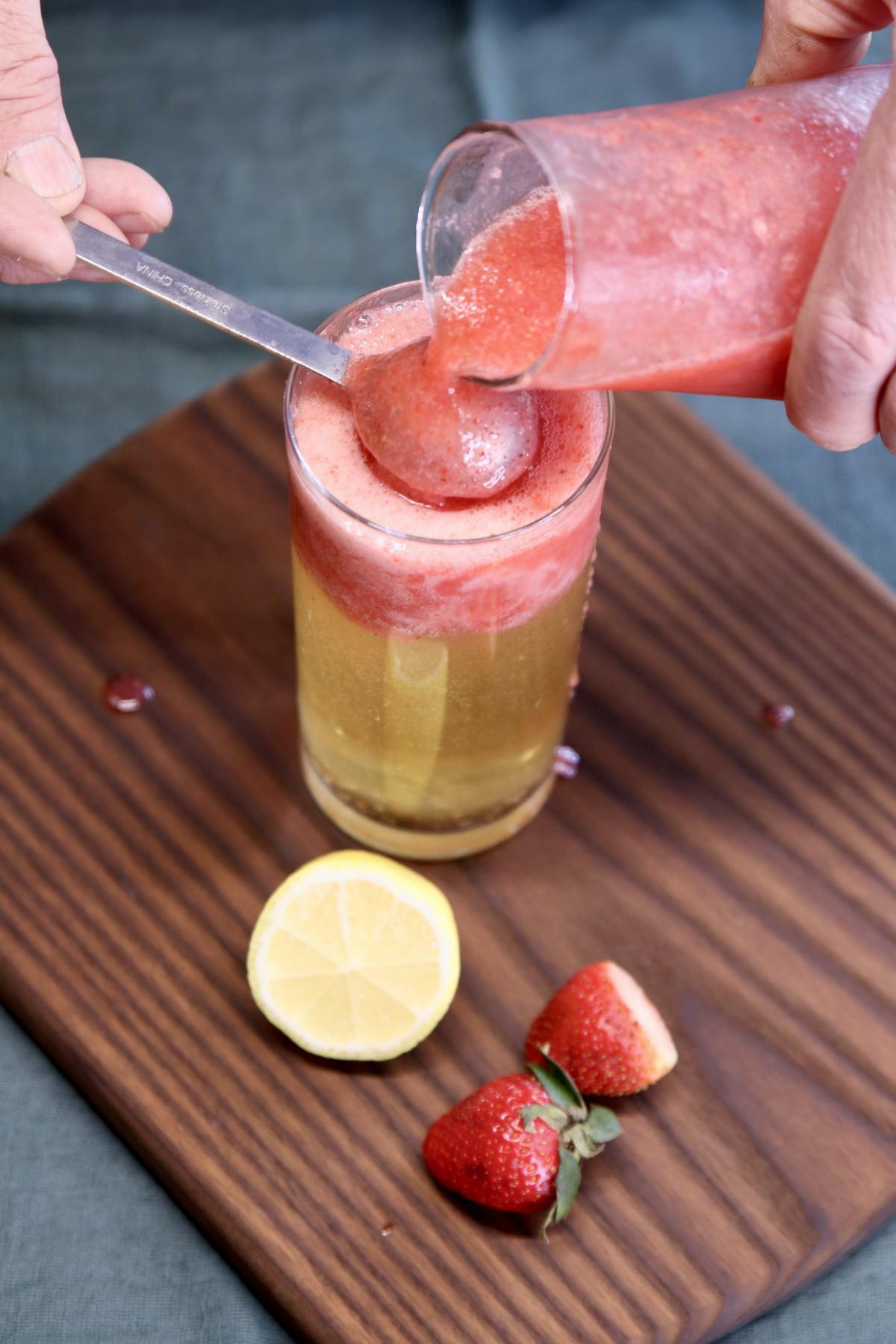 pouring strawberry mixture over a spoon into beer glass.