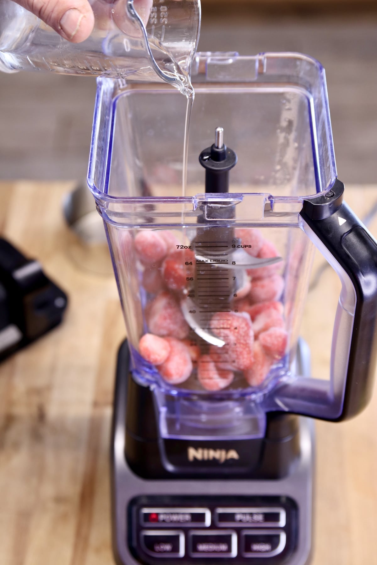pouring simple syrup into a blender with frozen strawberries.