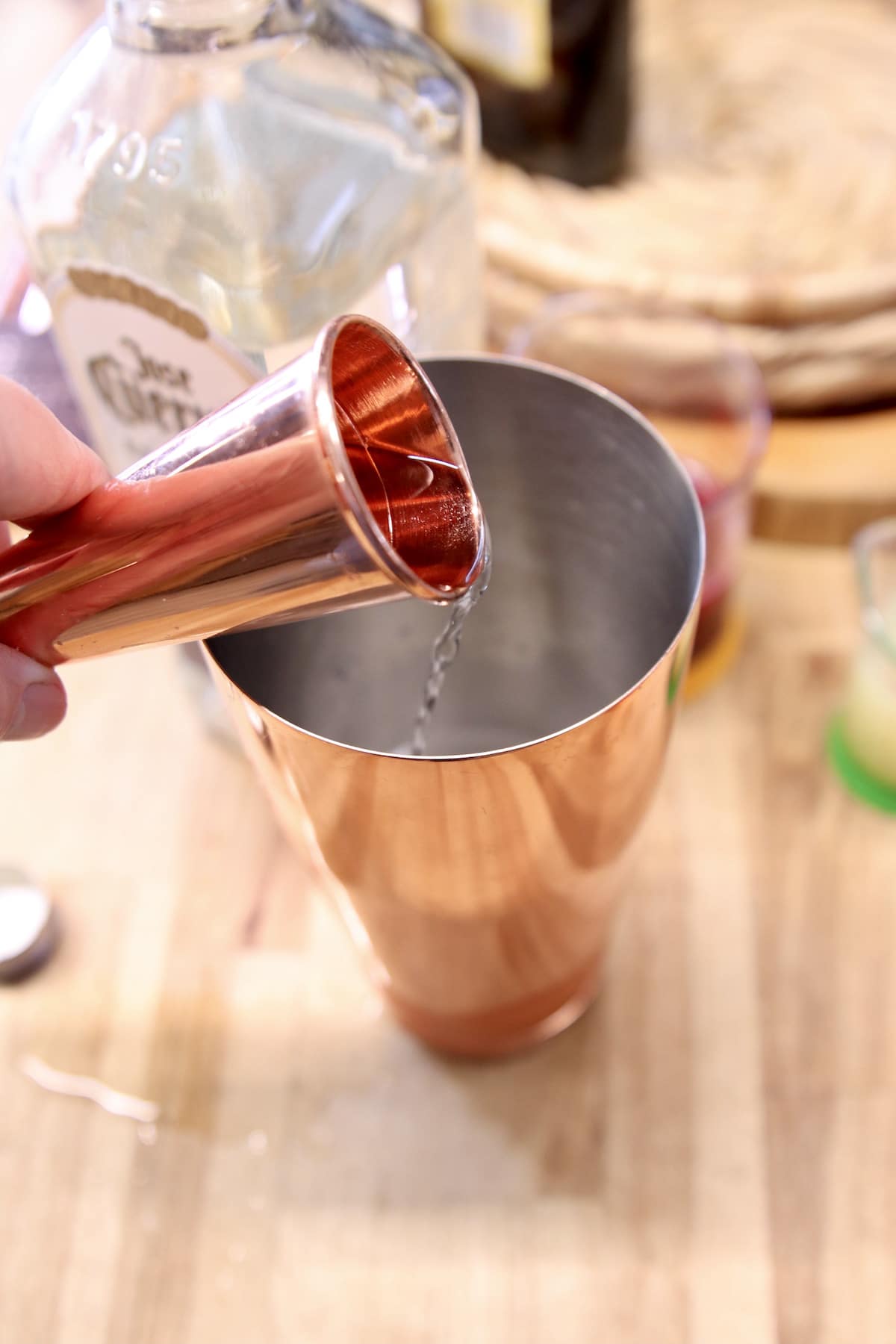Pouring tequila into cocktail shaker with copper jigger.