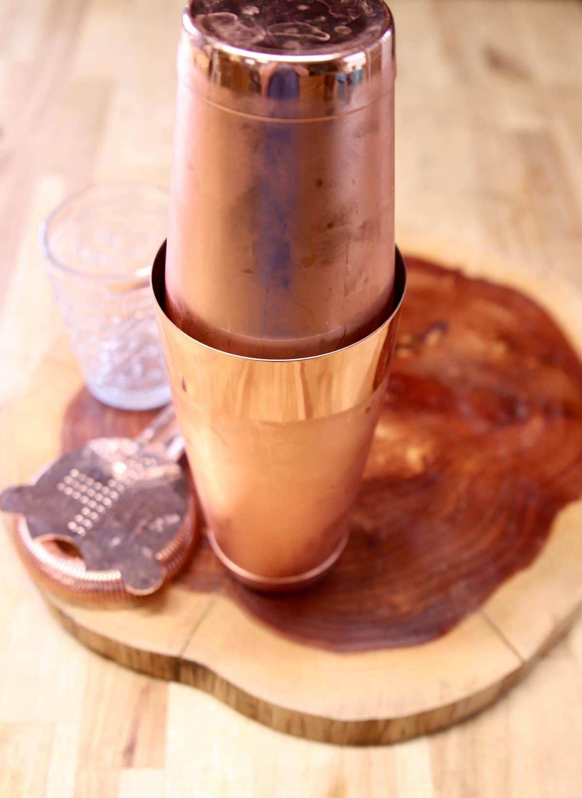 copper cocktail shaker on a board with strainer and glass.