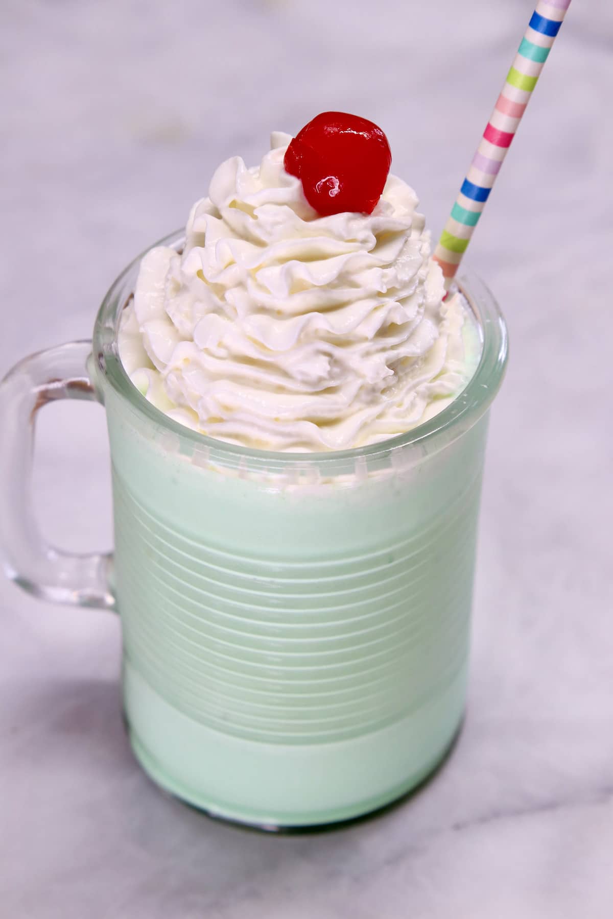 Mint shake with whipped cream, cherry and straw in a glass mug.