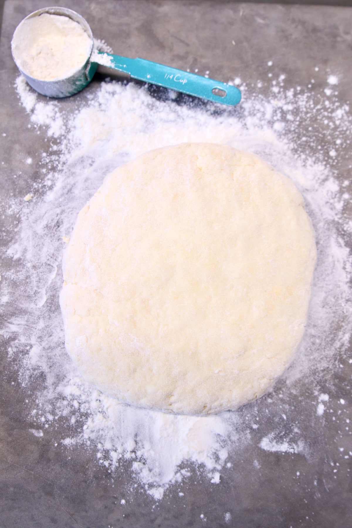 Soda bread dough on a floured surface with cup of flour.