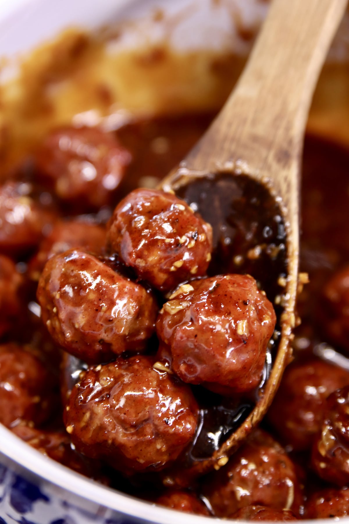Meatballs in honey garlic sauce in a pan with wooden spoon.
