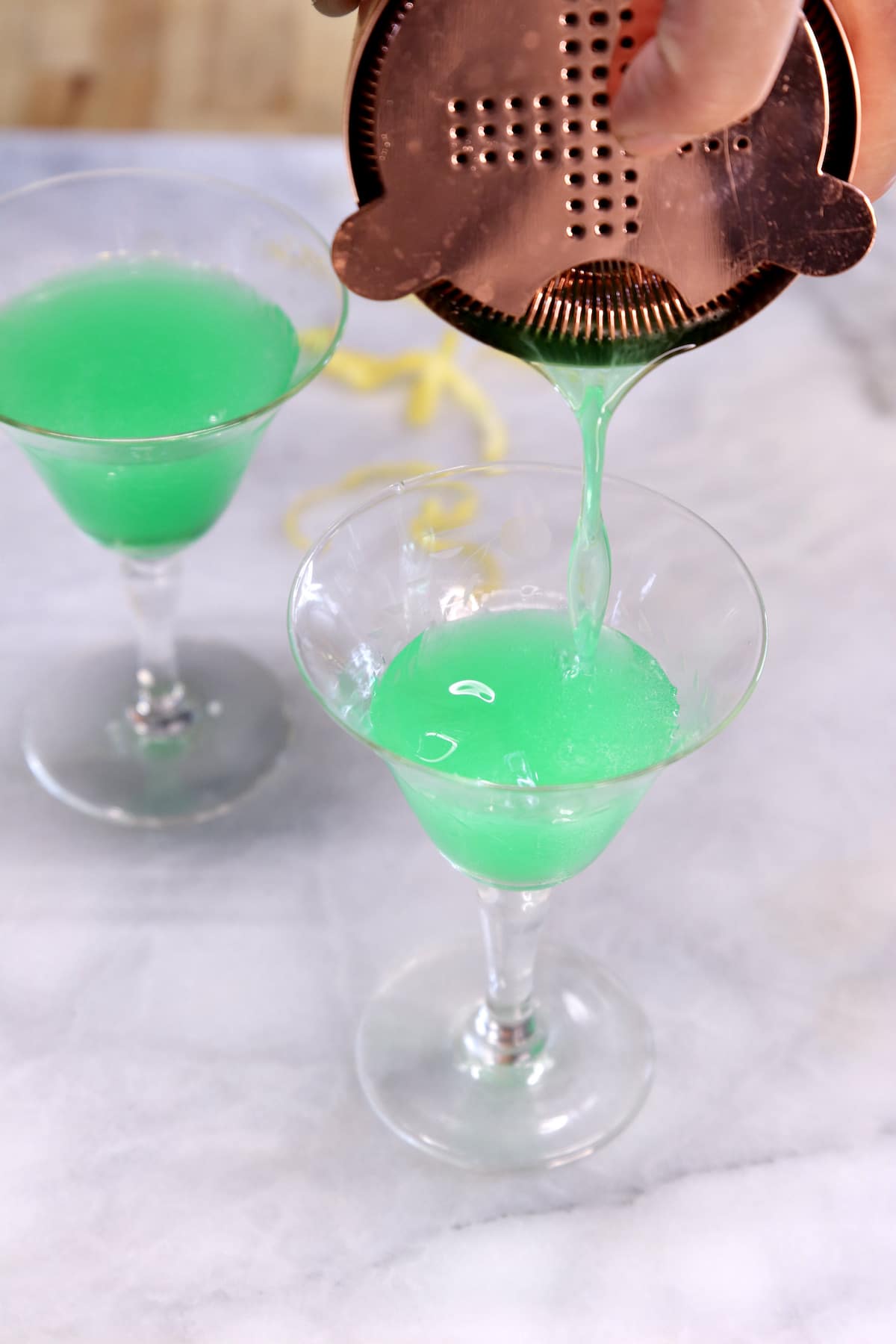 Pouring green martini into couple glasses.