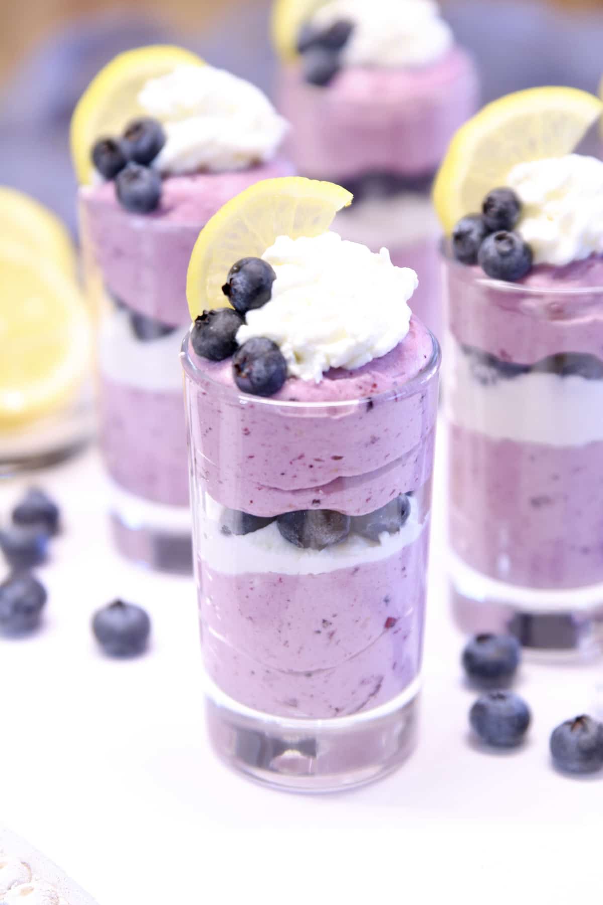 4 dessert glasses with layered blueberry cheesecake.
