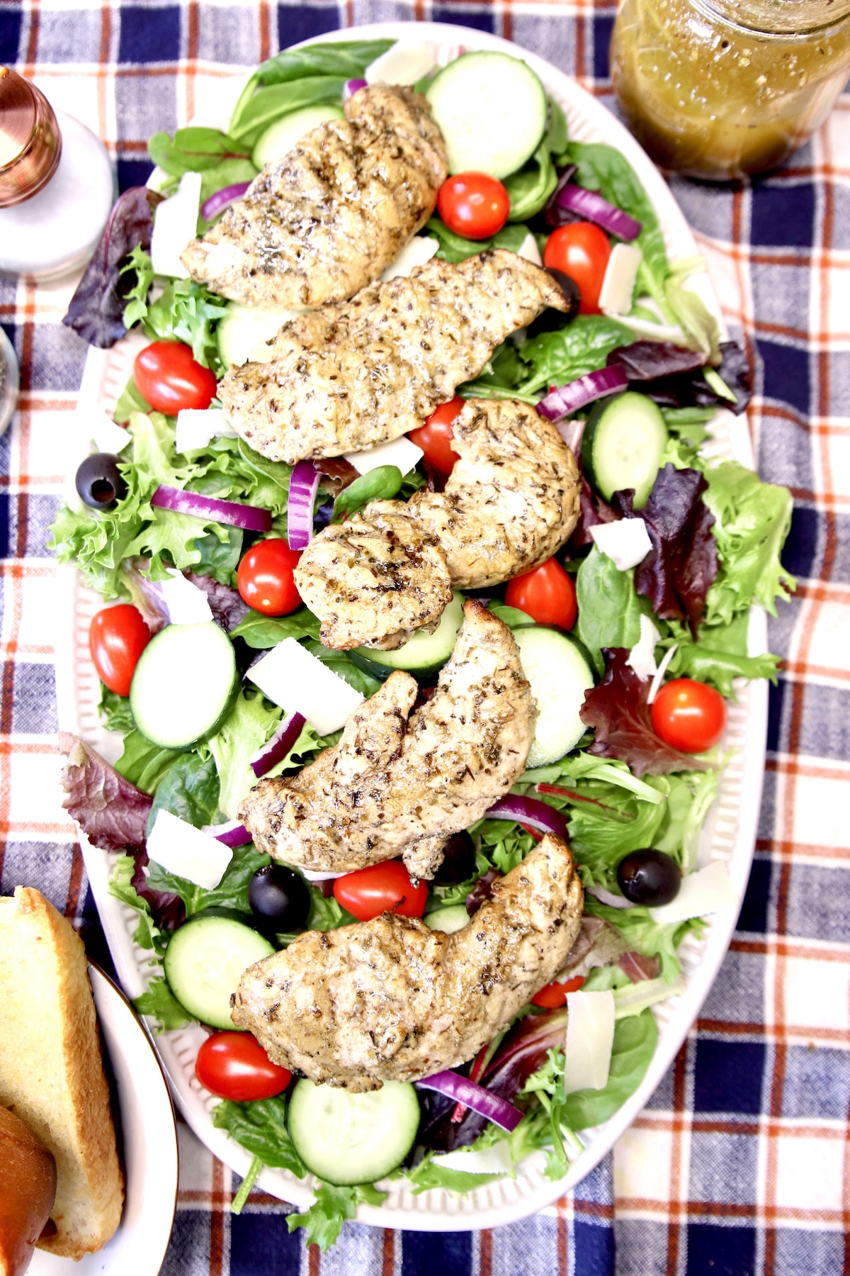 Overhead view of platter of salad with grilled chicken, tomatoes, cucumbers, black olives.