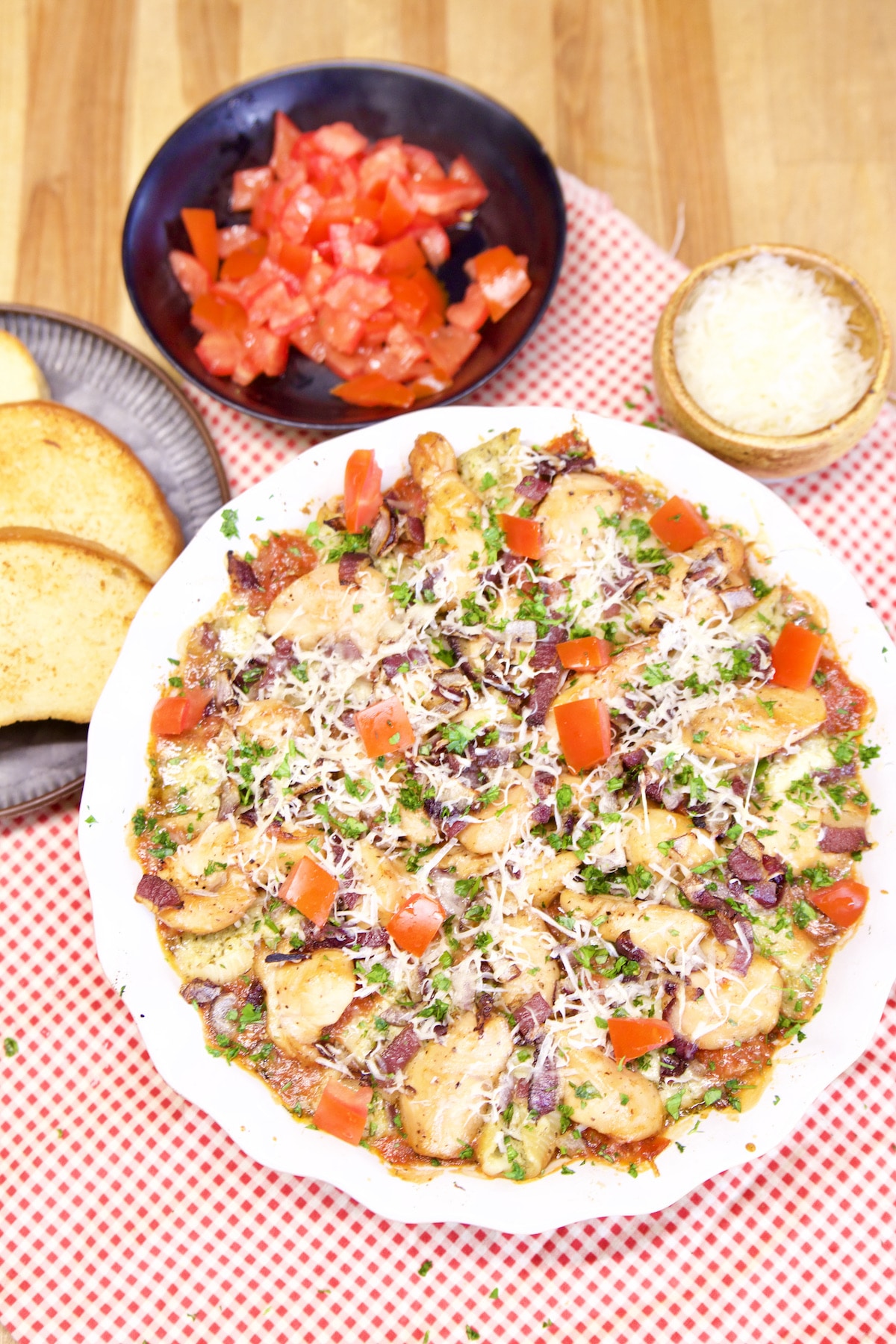 Chicken Stuffed Pasta casserole with bowl of tomatoes, parmesan and garlic bread.