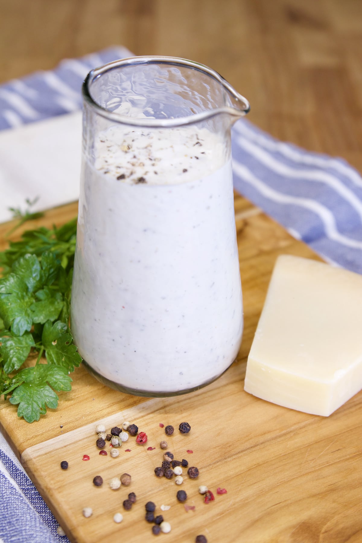 Glass pitcher with ranch dressing, peppercorns, parsley and parmesan cheese.