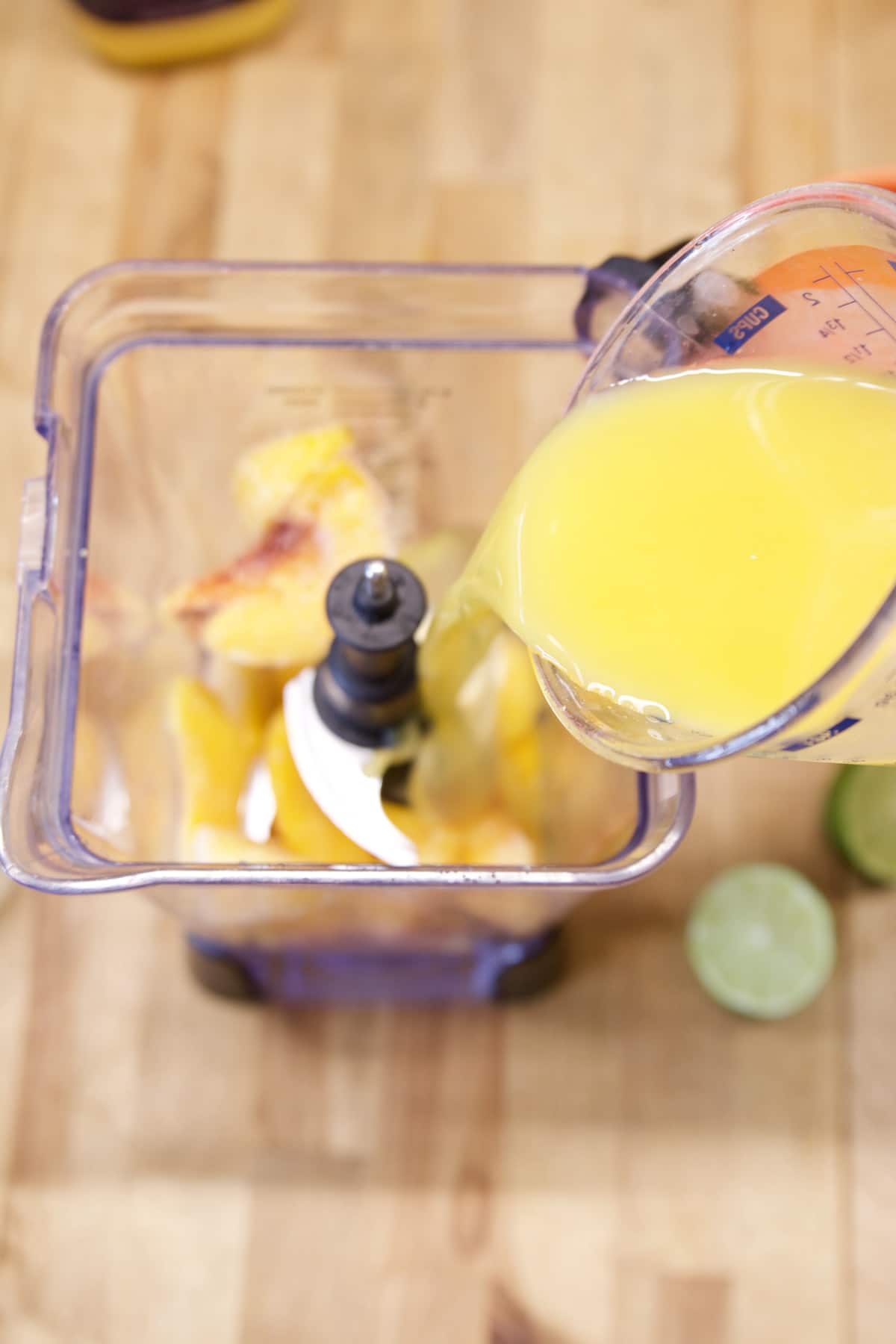 Pouring orange juice into a blender with peaches.