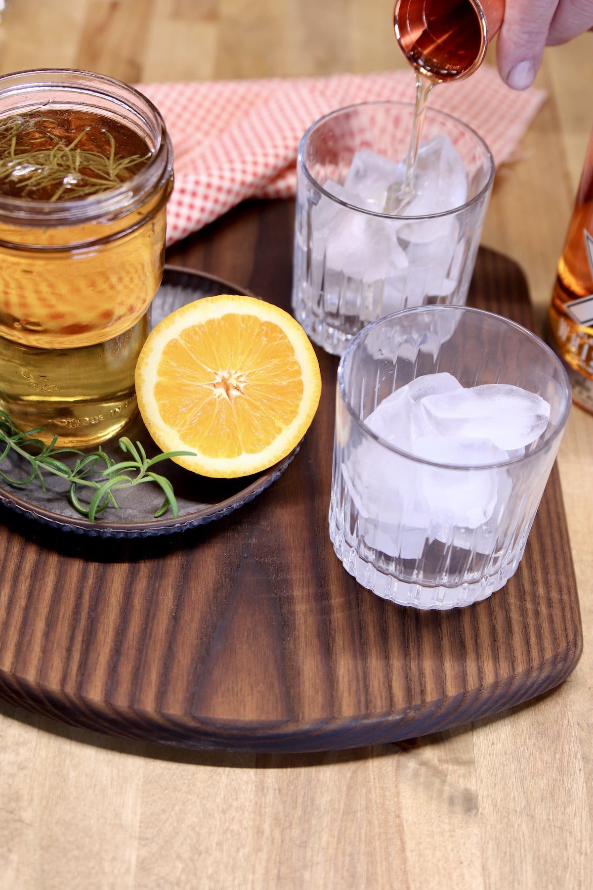 2 rocks glasses with ice, pouring simple syrup from jigger.