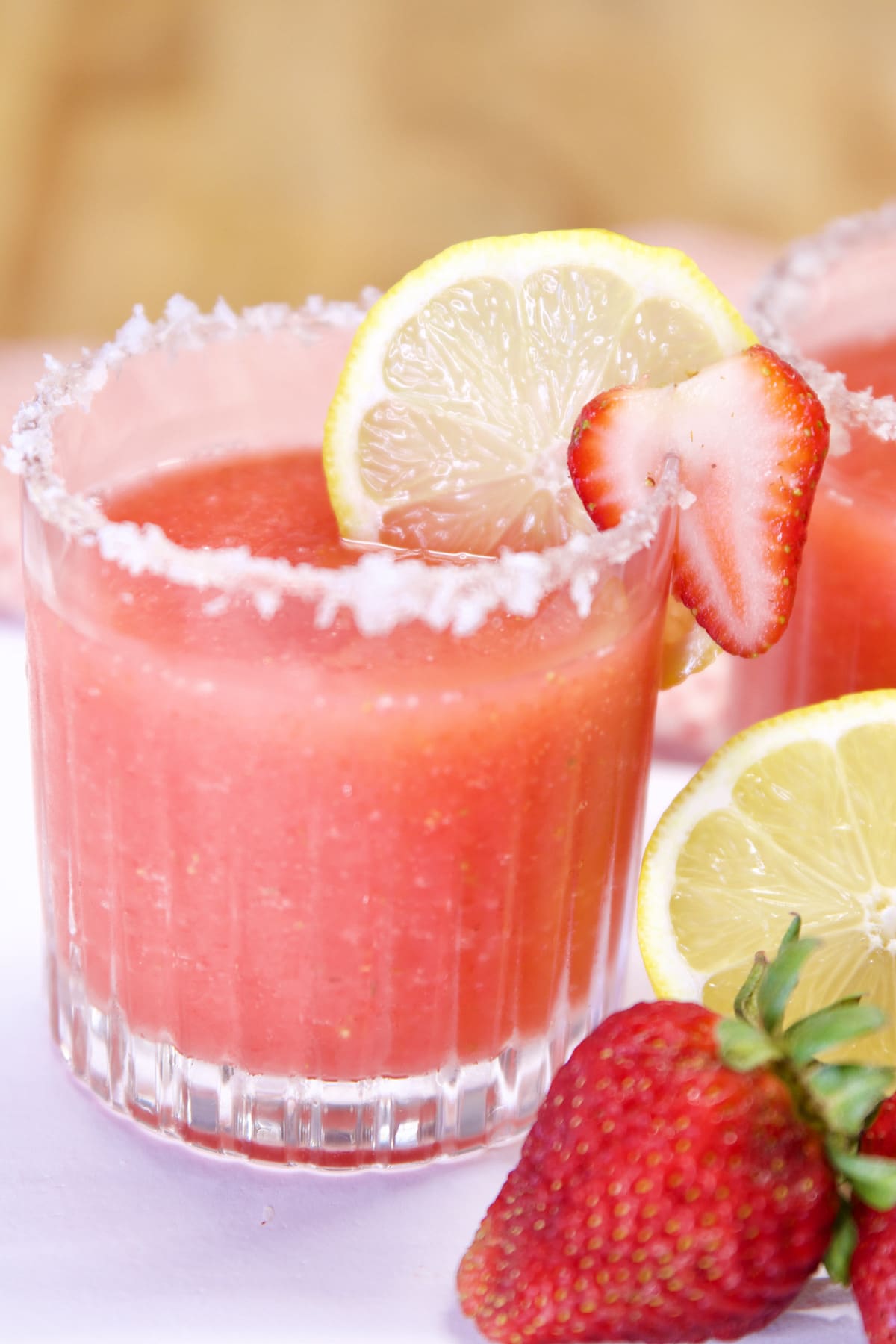 glass of strawberry margaritas with lemon and strawberry garnish.
