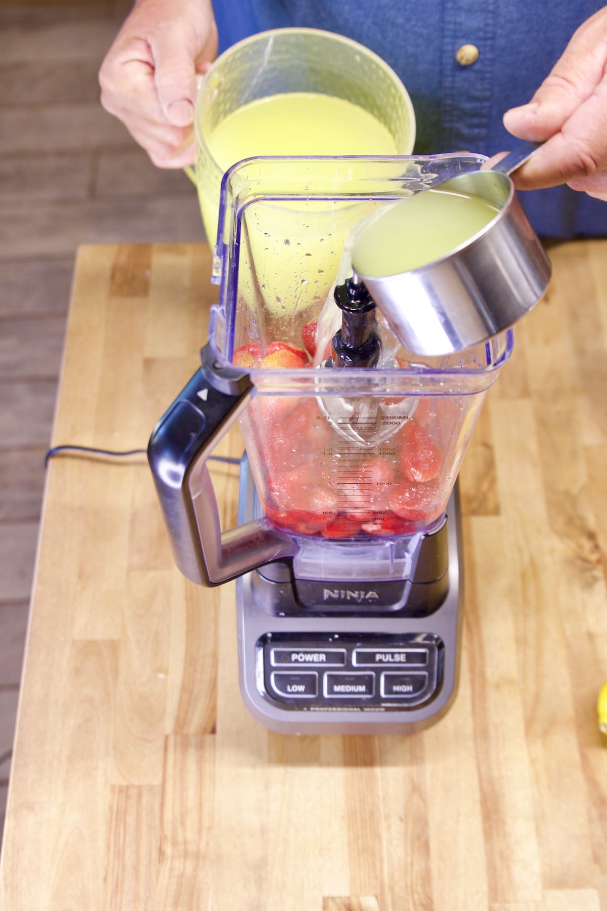 Pouring lemonade into a blender with strawberries.