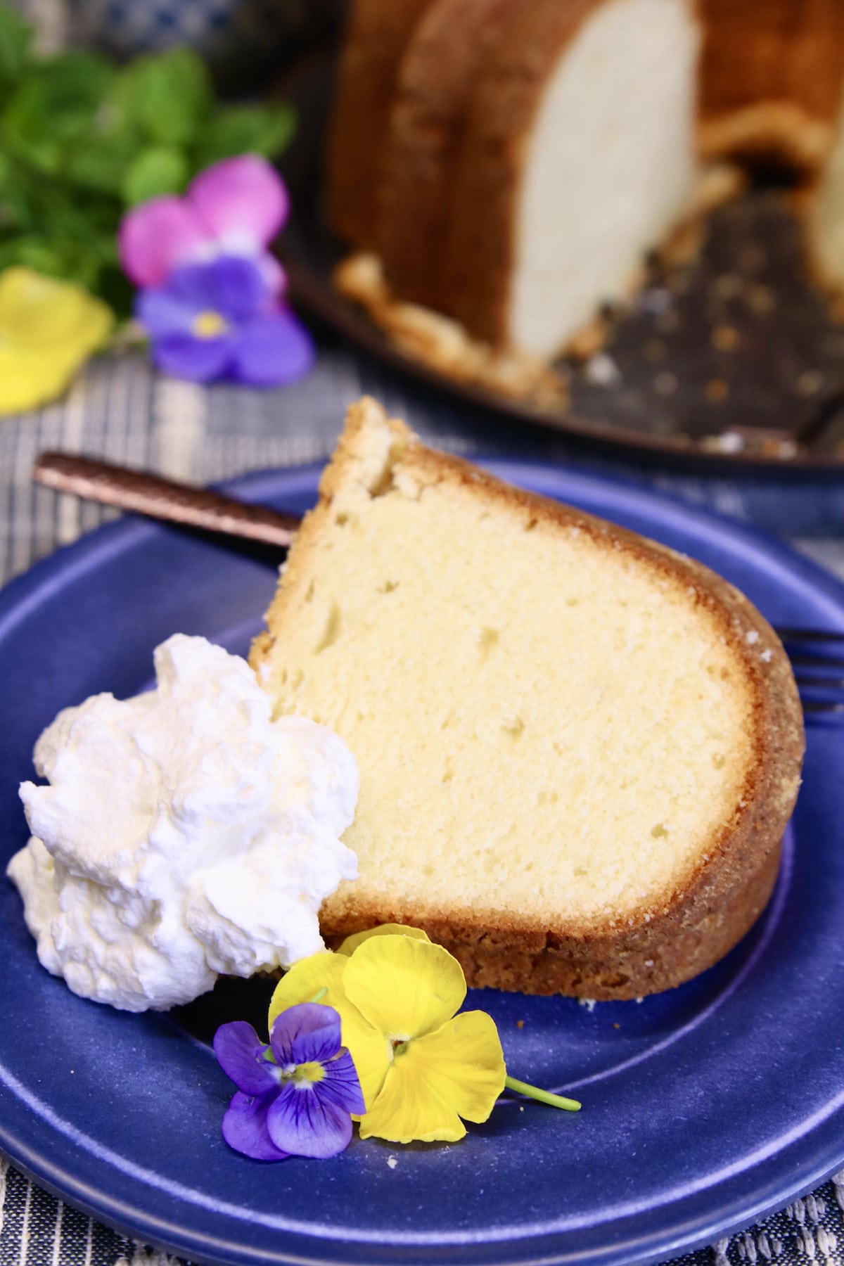 Slice of cream cheese pound cake on a blue plate with pansies.
