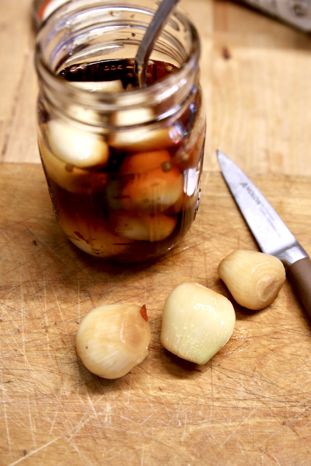 Pickled onions in a jar, 3 on a cutting board with a knife