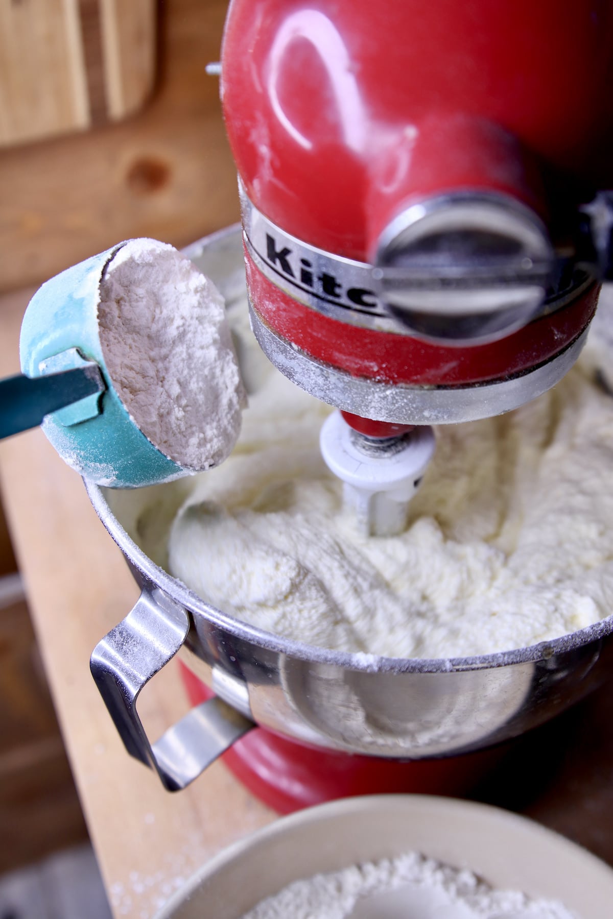 Adding flour to mixer bowl of cake batter using Kitchenaid mixer.