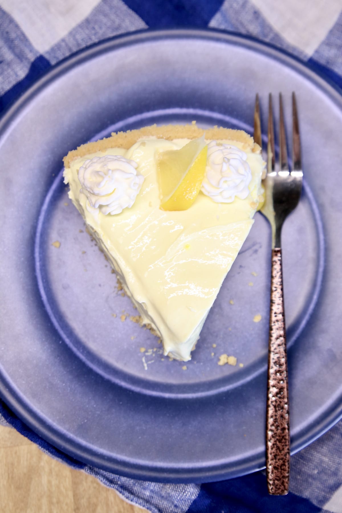 Slice of lemon pie on a blue plate with a fork.