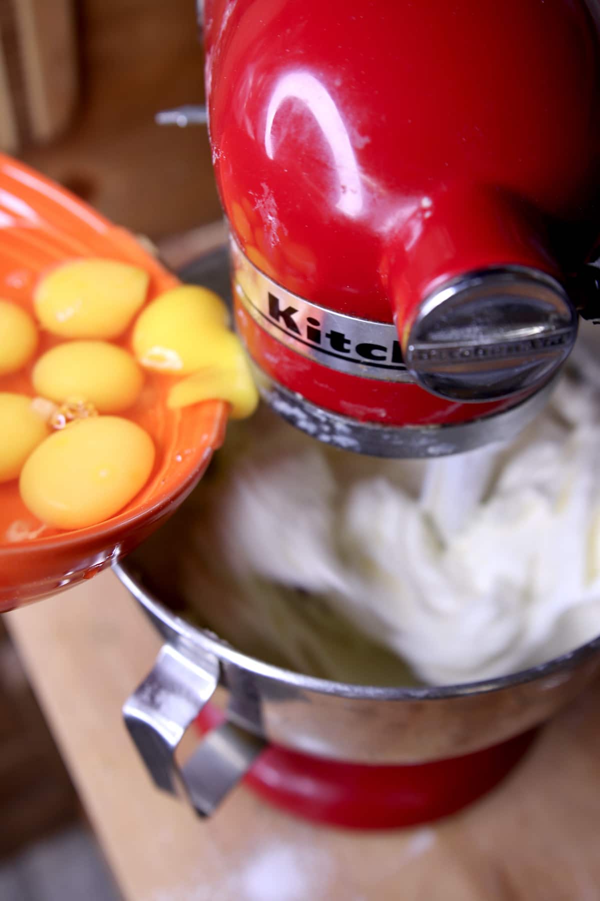 Adding eggs to cake batter in red Kitchenaid Mixer.