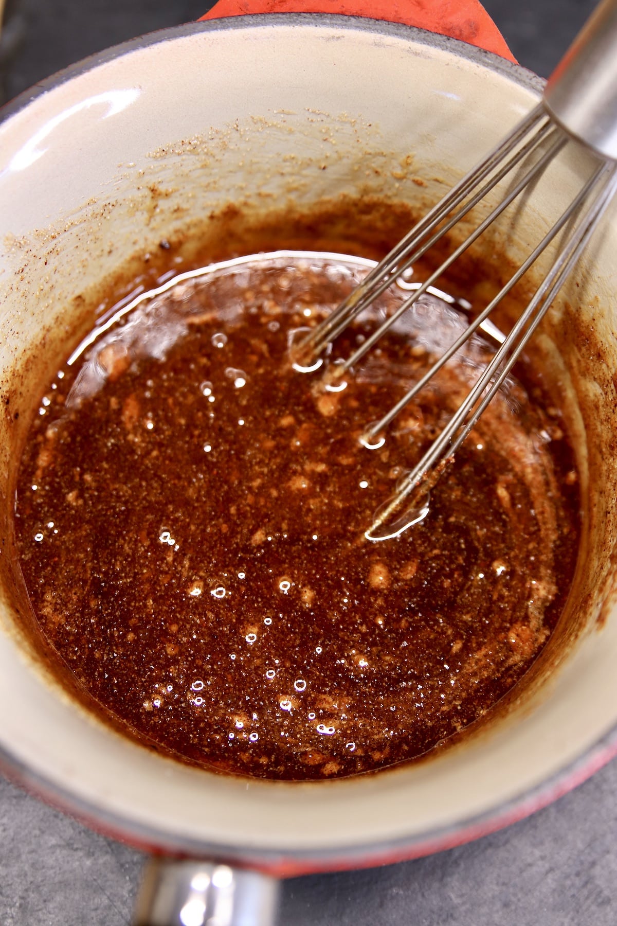 Honey garlic sauce in a saucepan with a whisk.