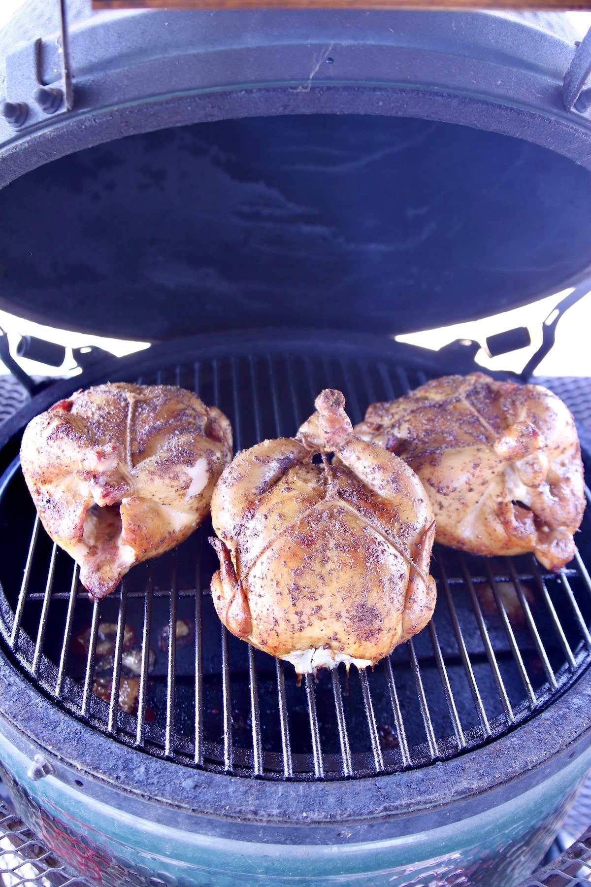 3 smoky whole chickens on a grill.