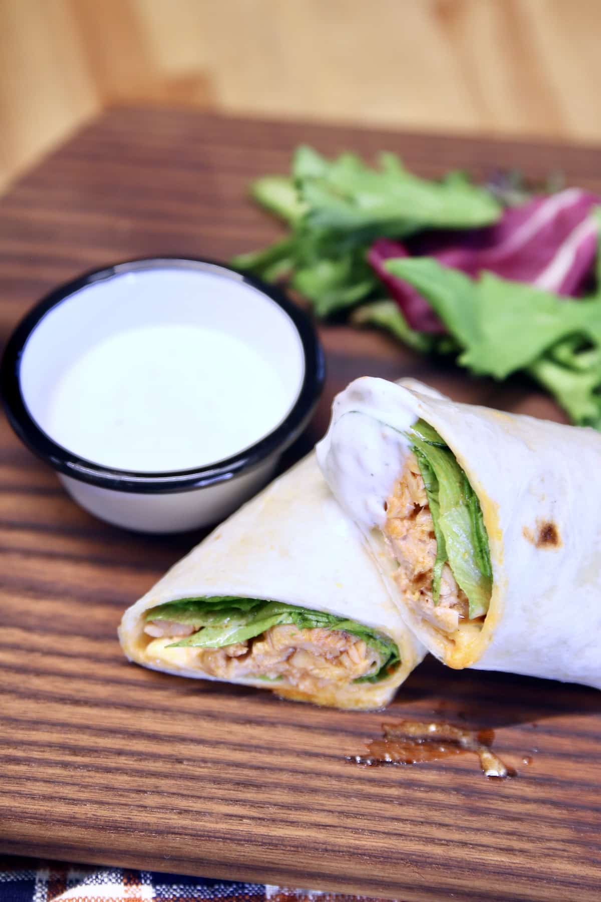 Chicken wraps with ranch dressing on a brown board.
