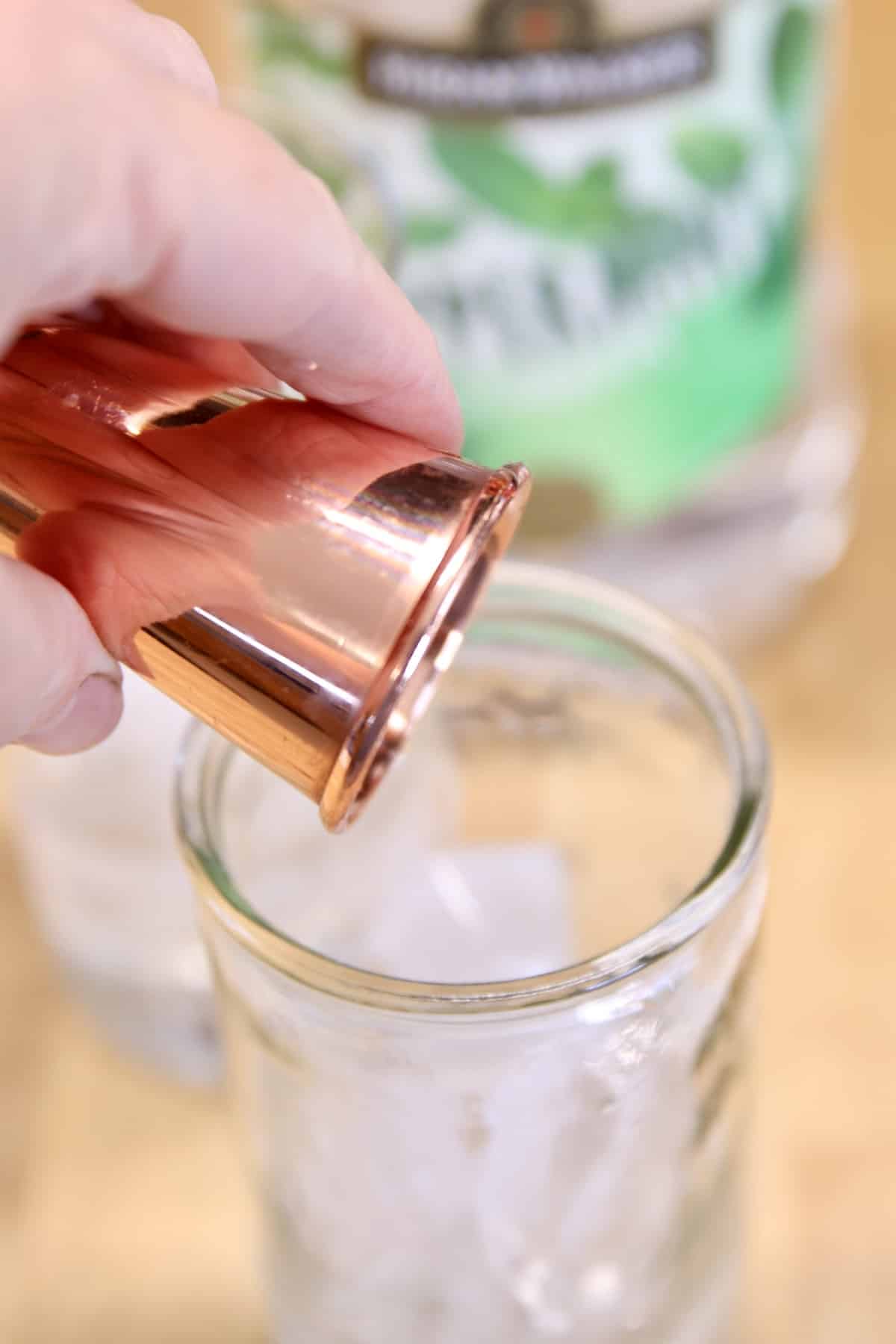 Pouring peppermint schnapps into a glass of ice.