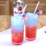 Red white and blue rum slush in 2 glasses, bottle of rum.