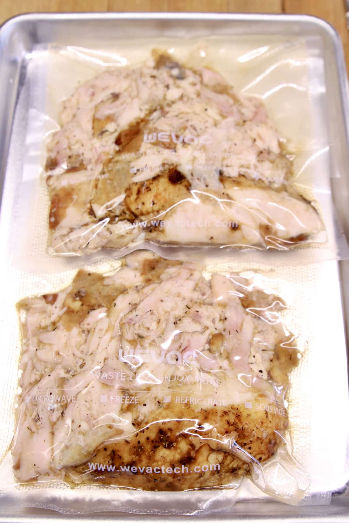 2 packages of vacuum sealed chicken on a sheet pan.