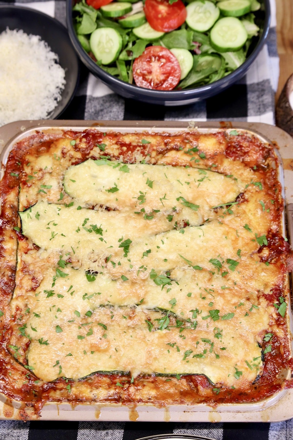 Zucchini lasagna in a pan, bowl of salad.