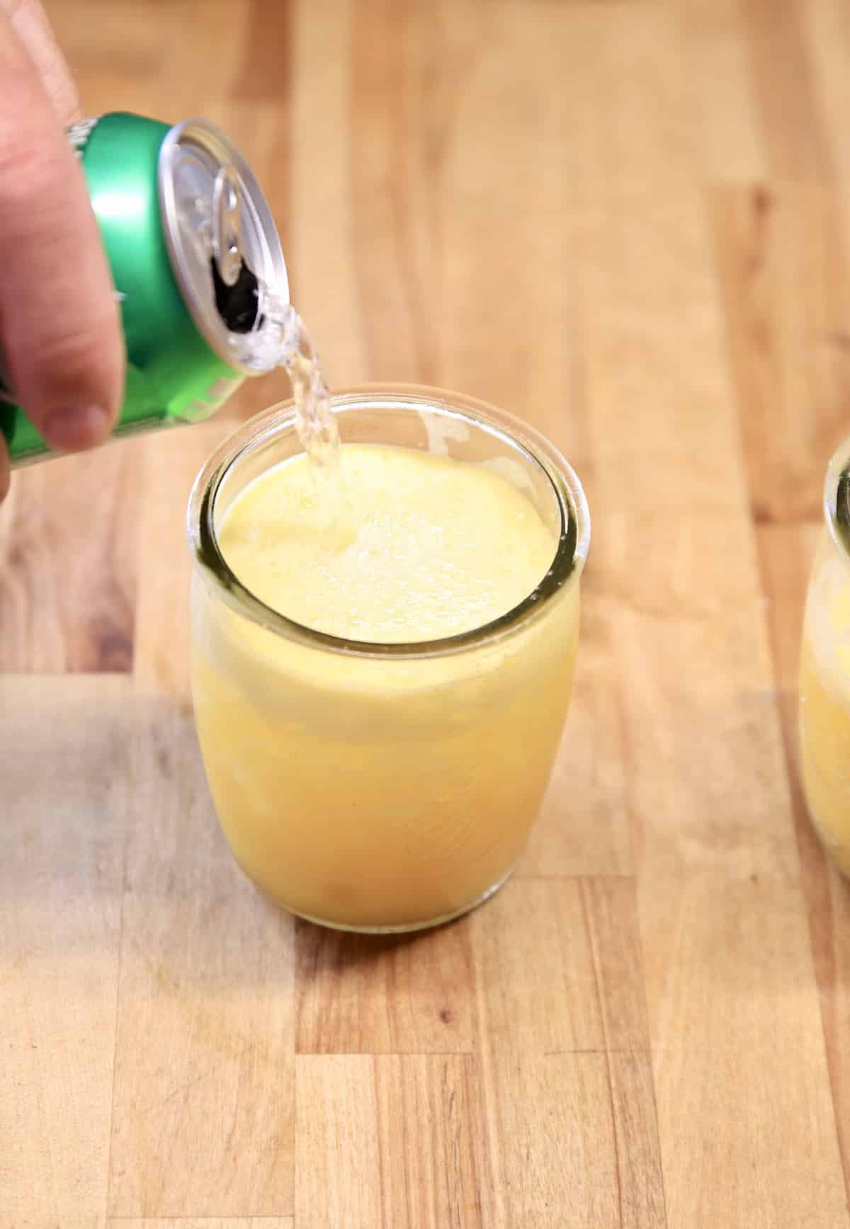 Pouring sprite over pineapple cocktail.
