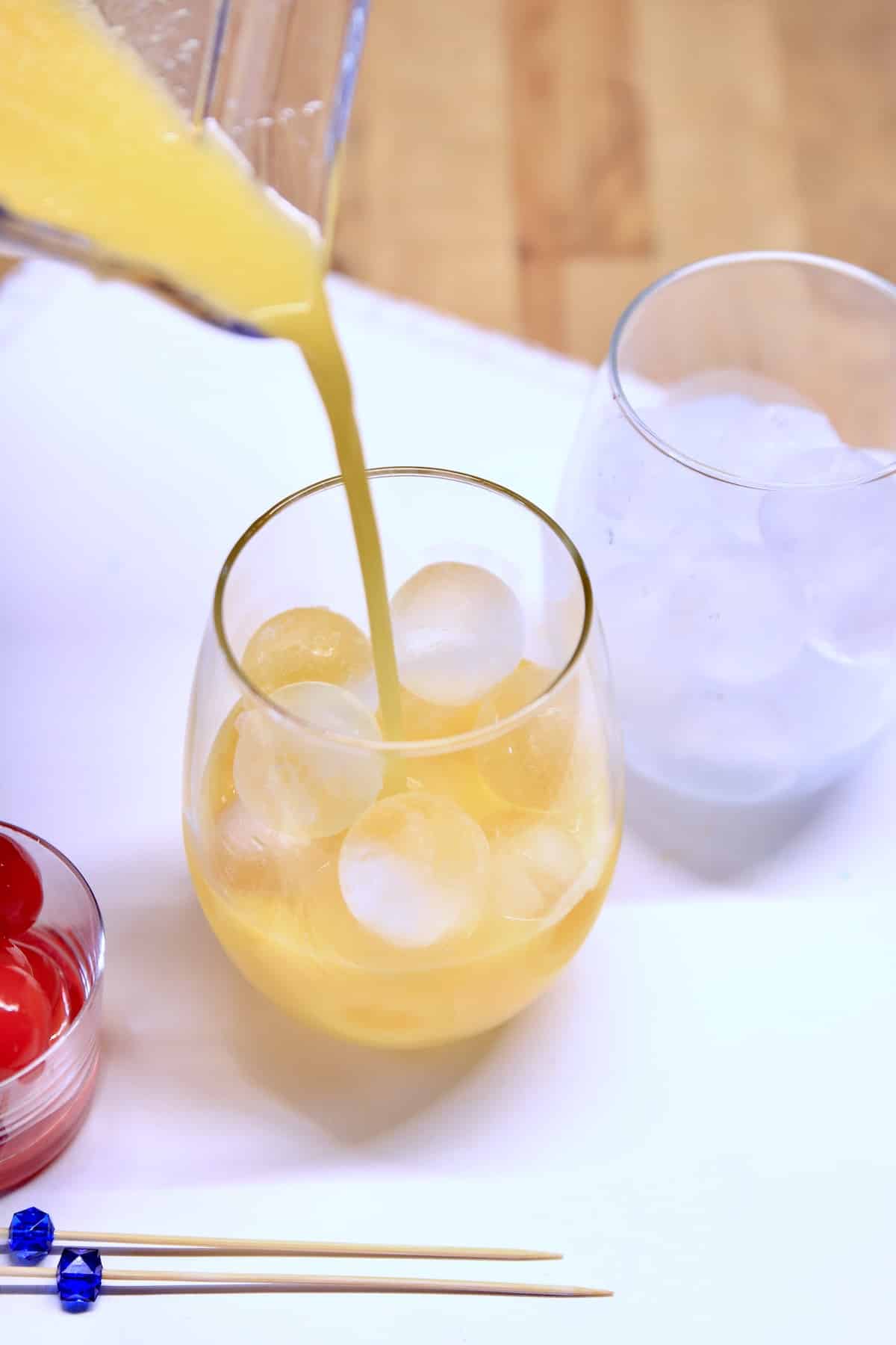 Pouring mango cocktail into glasses with ice.