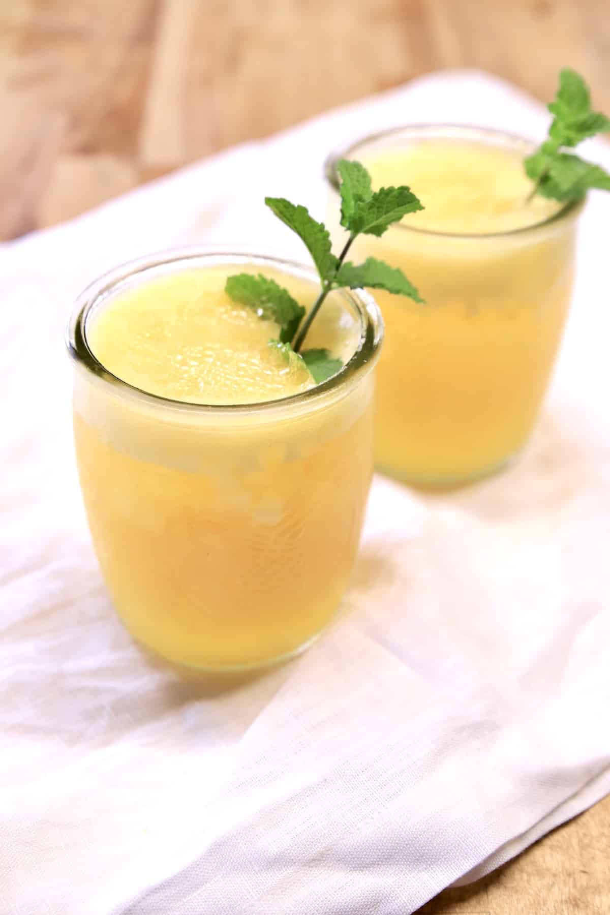 2 pineapple mango cocktails in glasses with mint garnish.