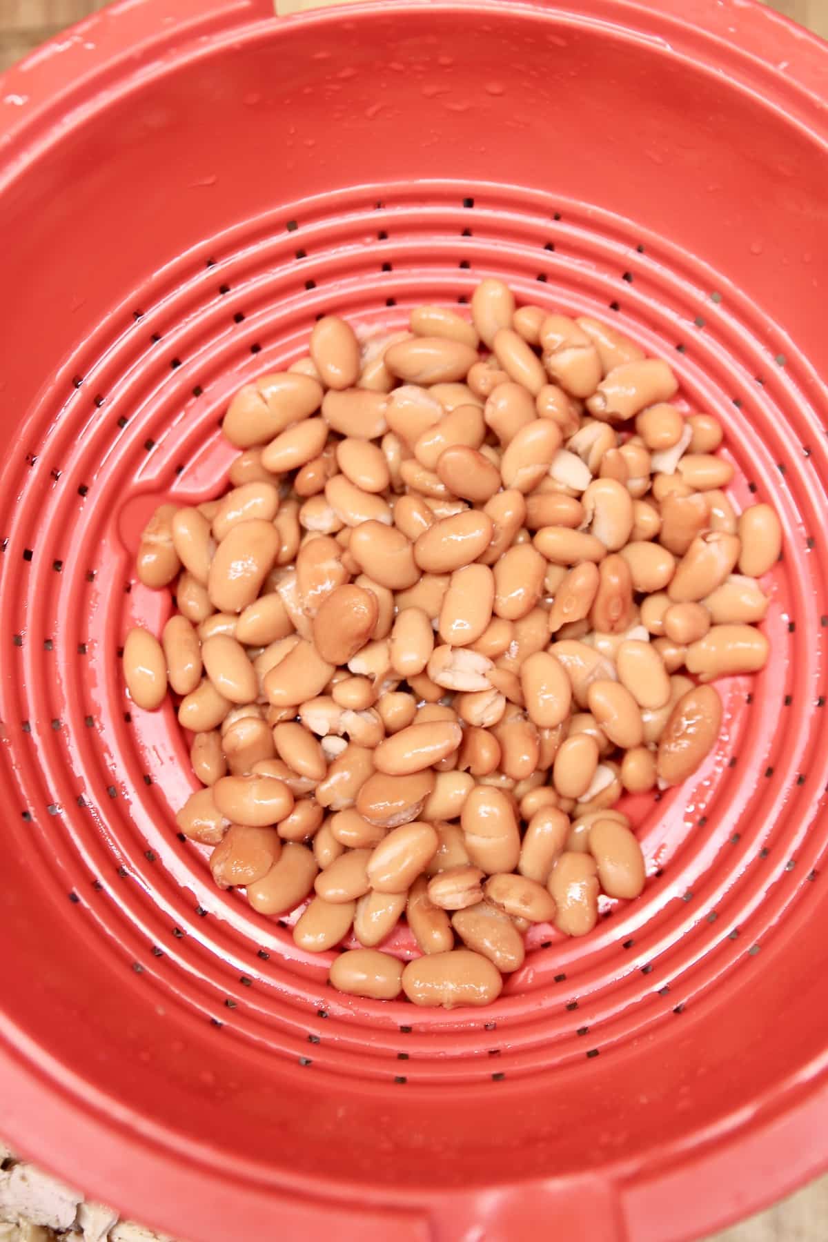 Drained pinto beans in red colander.