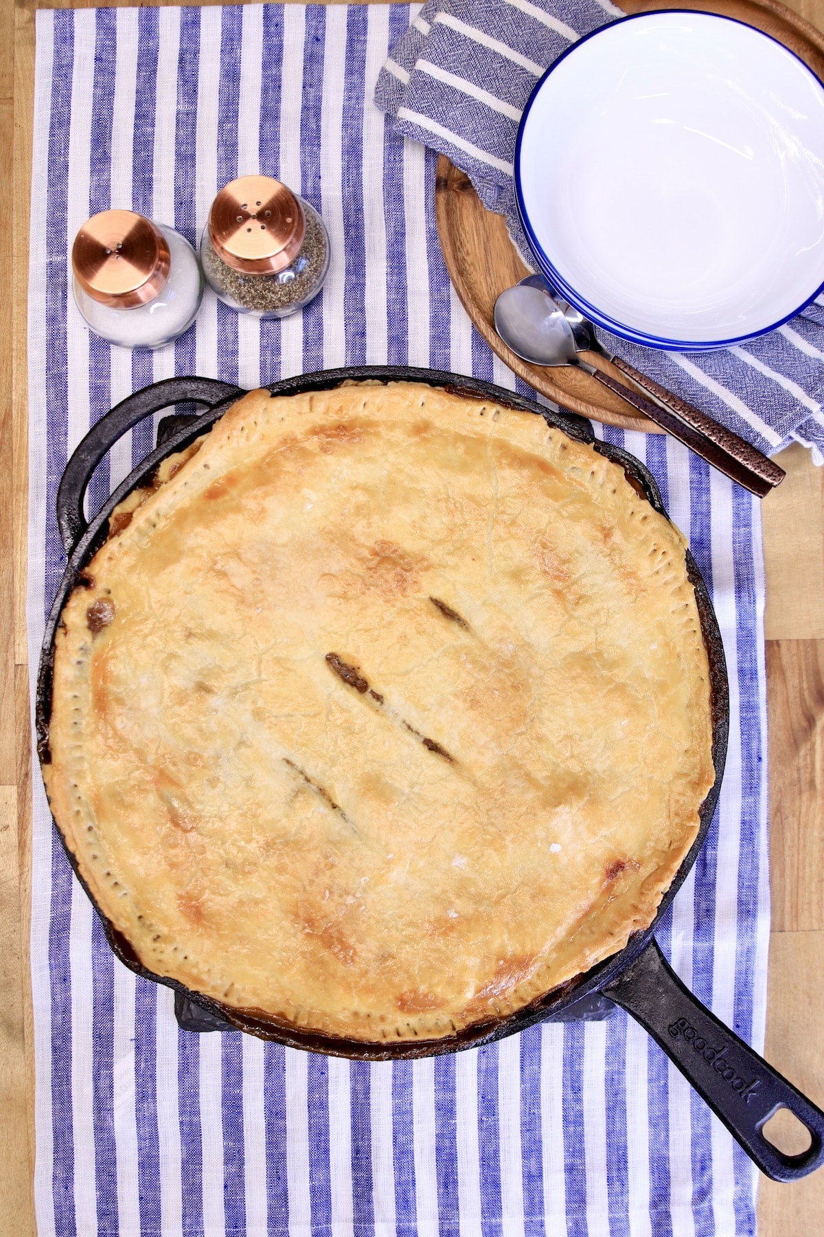 Skillet pot pie on a striped table cloth, plates on the side.