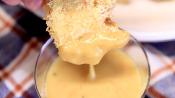Chicken nugget dipping into yellow sauce.