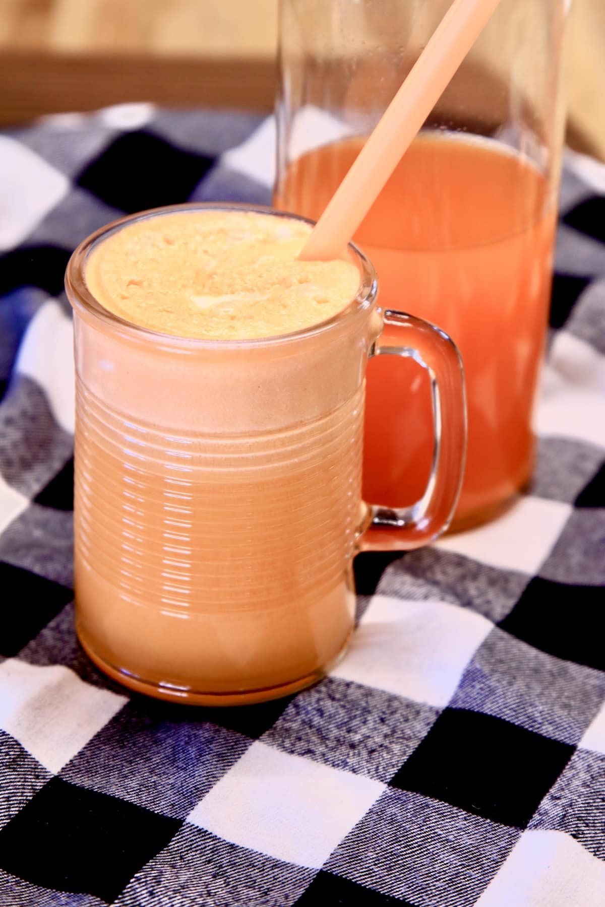 Orange punch in a mug with straw, pitcher in background.