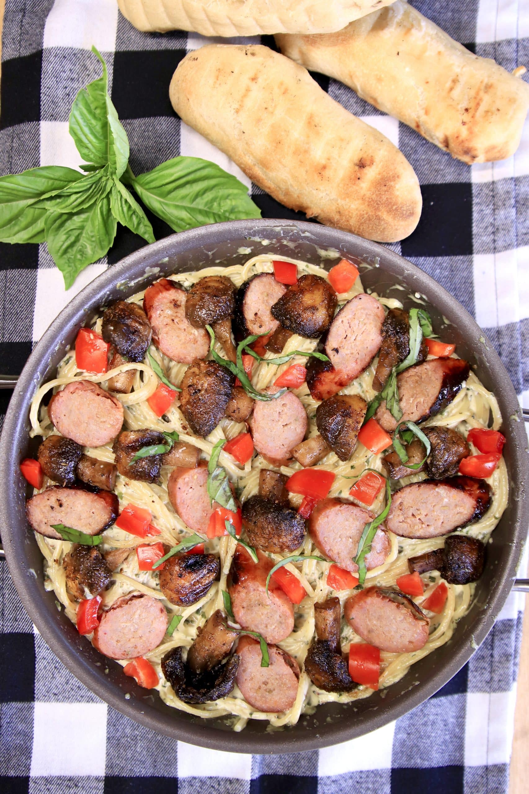 Pan of pasta with sliced sausage links, tomatoes, basil.
