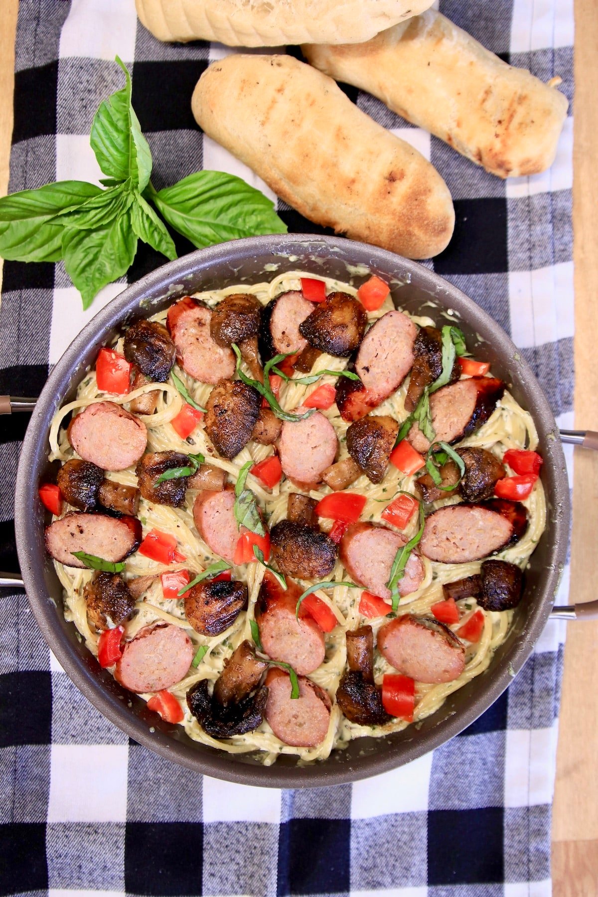 Pan of grilled sausage and mushroom pasta with breadsticks.