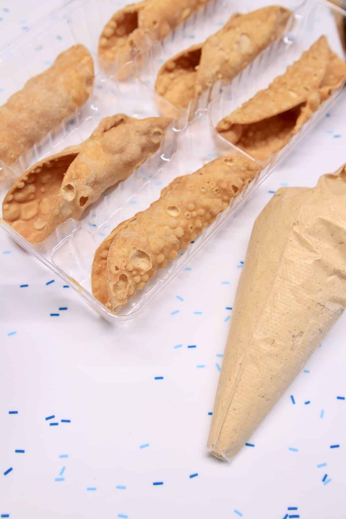 Cannoli shells with piping bag of pumpkin filling.