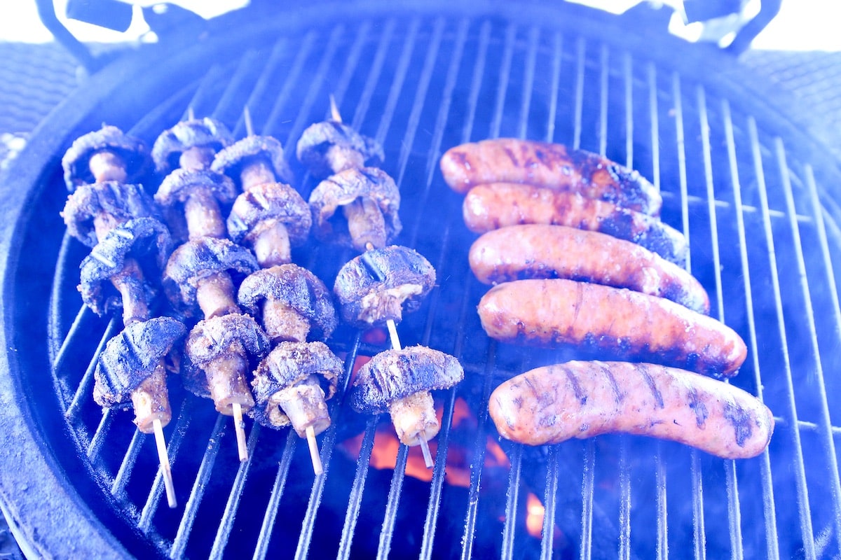 Mushrooms on skewers and Italian sausages on a grill.