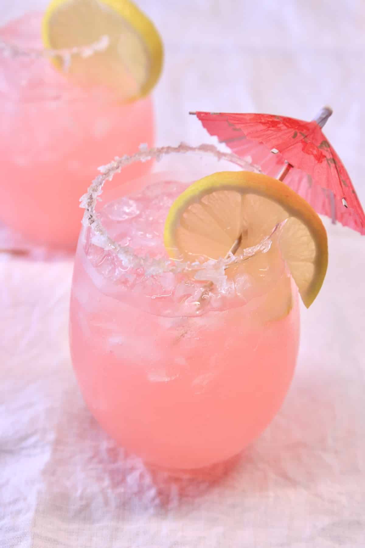 2 stemless wine glasses with pink margaritas. Drink umbrella and lemon wheel garnish.
