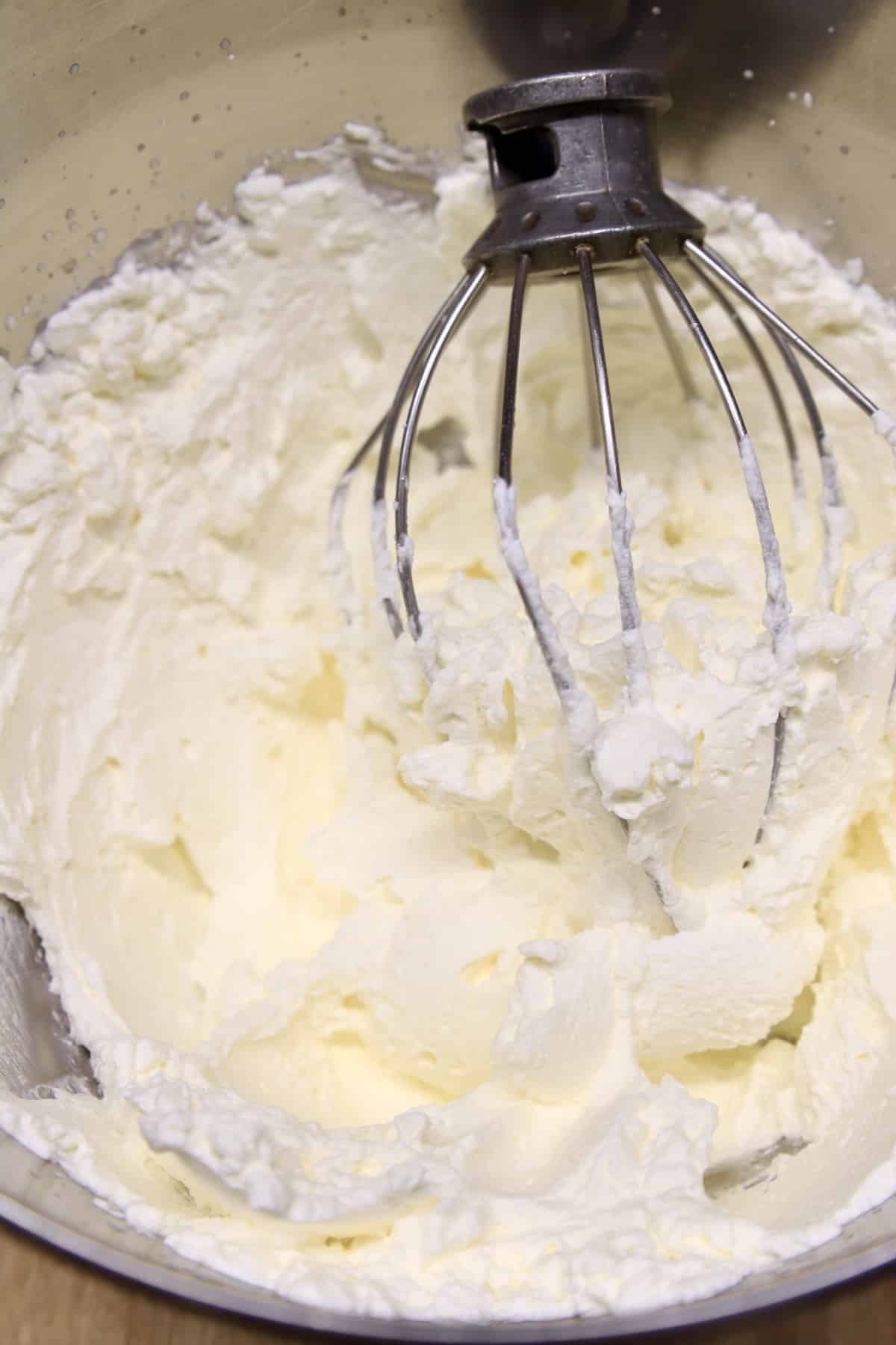 Whipped cream in a bowl with beater whisk.